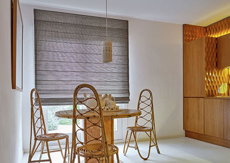 A dining room features a round table and unique curved woven chairs next to shades for sliding glass doors