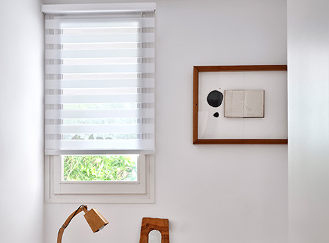 Double Roller Shades for windows cover a small window in a minimalist-styled bedroom with a simple piece of wall art