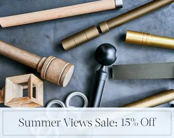 Pieces of drapery hardware in metal & wood finishes lay on a stone table with sales messaging for Summer Views Sale: 15% Off