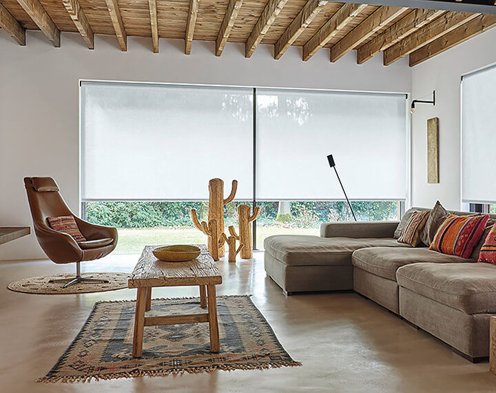 A living room with natural accents and large windows dressed with 3% thermo cloud energy efficient Roller Shades.