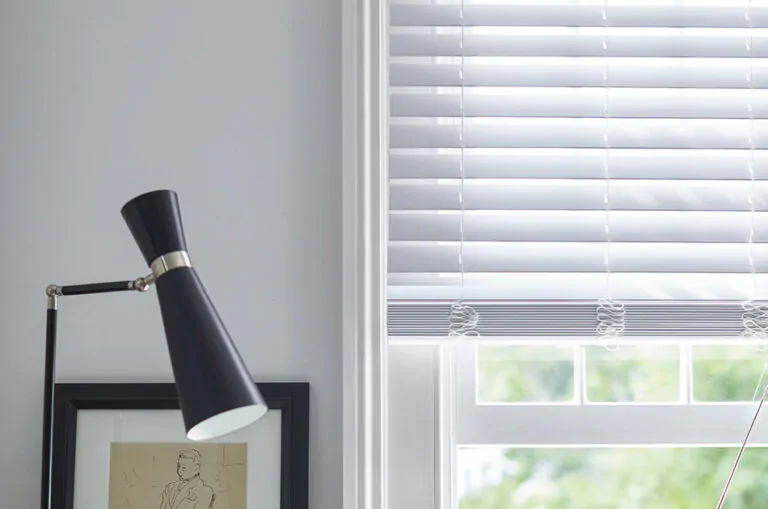 An image to answer what is faux wood shows 2-inch Faux Wood Blinds in Blanc next to white walls and black decor