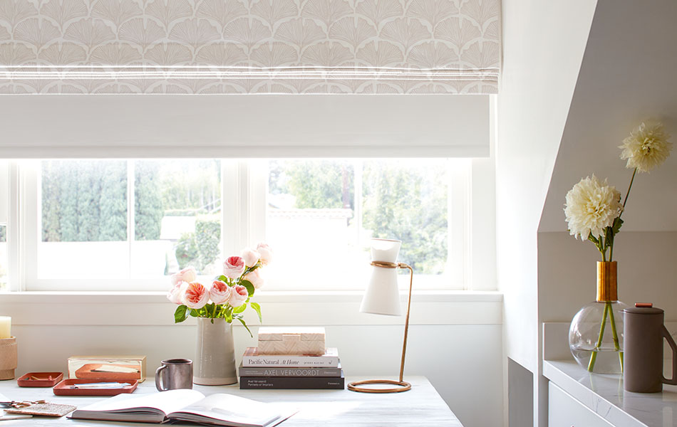 A cozy office with off-white colors has a Flat Roman Shade made of Feather Palm in Waverly White over a blackout Roller Shade