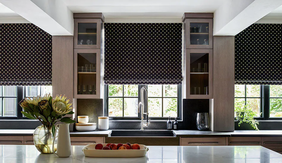 A modern kitchen has motorized cordless Roman Shades made of Nate Berkus Gemma in Noir over windows above the counter