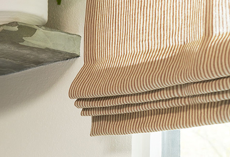 A close up of a Roman Shade made of Nate Berkus Lisbon Woven in Bronze shows the stack of the folded fabric