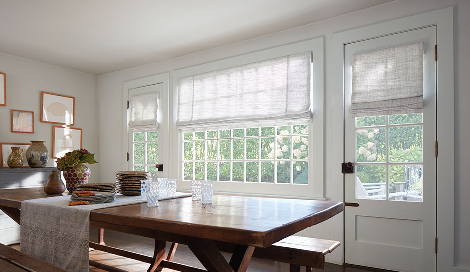 A dining room has cordless Roman Shades made of Shoreline in Cloud that add a texture while complementing the white walls