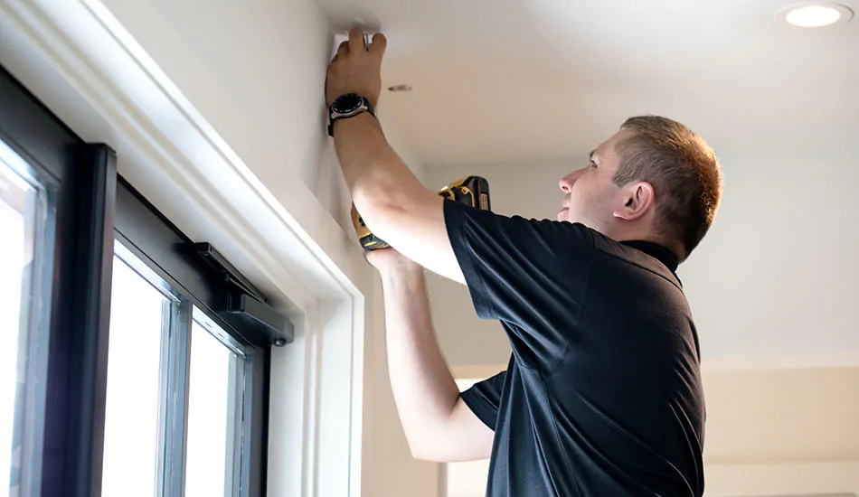 A professional window treatment installer carefully marks where a bracket should be installed on the ceiling above a window