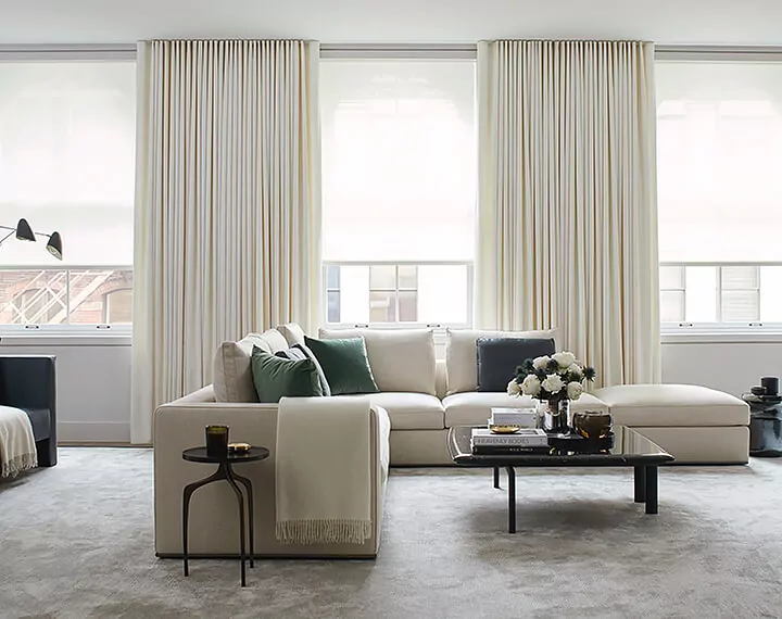 A living room with a white couch and large windows dressed with white motorized Drapery & Solar Shades.