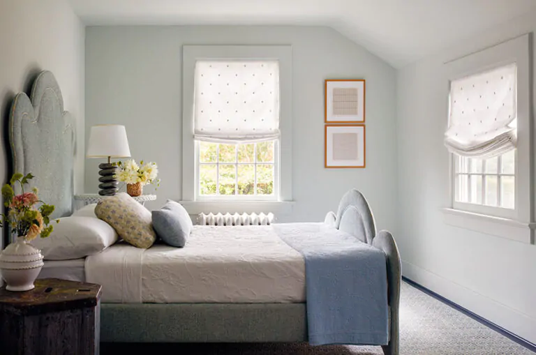 A bedroom shows tips for how to brighten a dark room including light filtering Relaxed Roman Shades made of Celeste in Moon