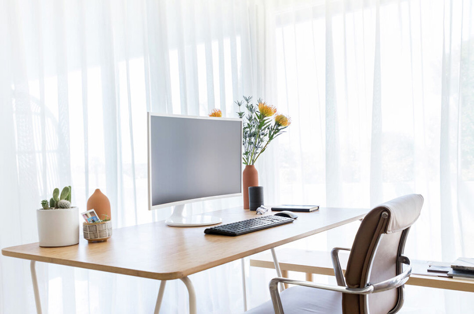 Home office curtains made of Sheer Elegance in Winter cover a corner window with a minimalist desk in front of it