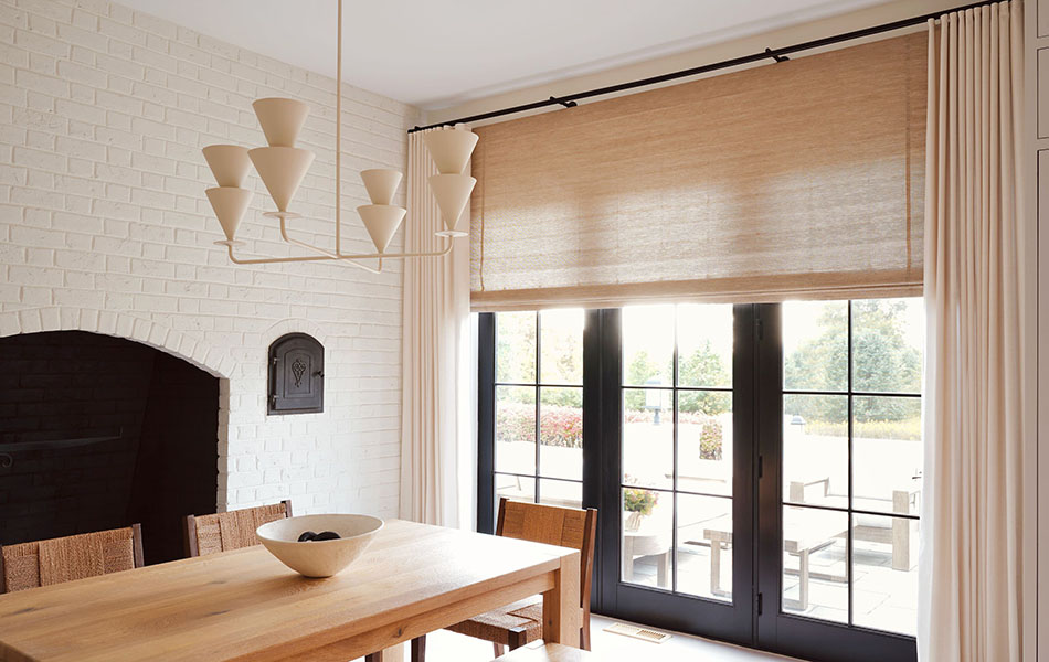 Dining room curtain ideas like woven shades layered with textured linen drapes create an organic look