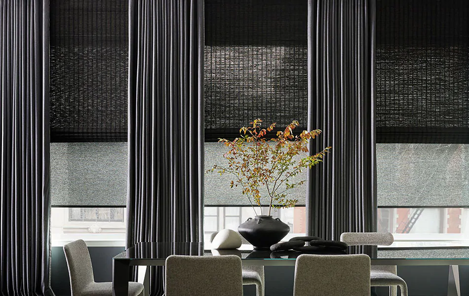 A modern dining room has layers of dark grey window treatments including Drapery, Woven Shades and Solar Shades