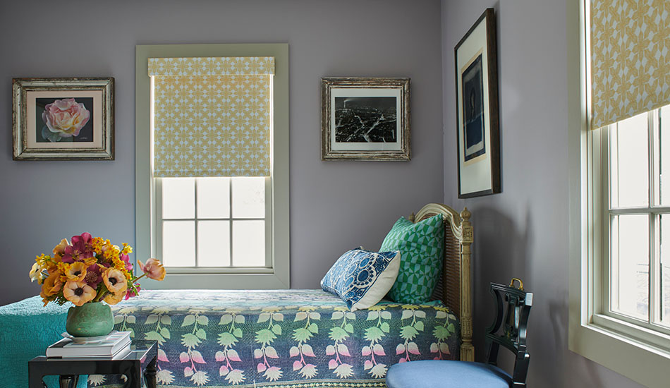 A Colorful bedroom with lavender walls has blackout Roller Shades made of Sheila Bridges Porringer in Mimosa