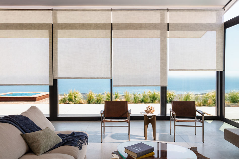 Light-filtering shades for sliding glass doors in a modern home are partially raised to allow a view of the seaside