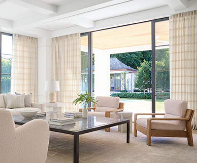 A living room with warm cream colors has drapery made of Victoria Hagan Lily in Buff over sliding glass doors