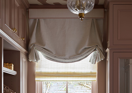 A Tulip Roman Shade made of Luxe Linen in Oyster adds whimsy and elegance to a dressing room with mauve cabinets