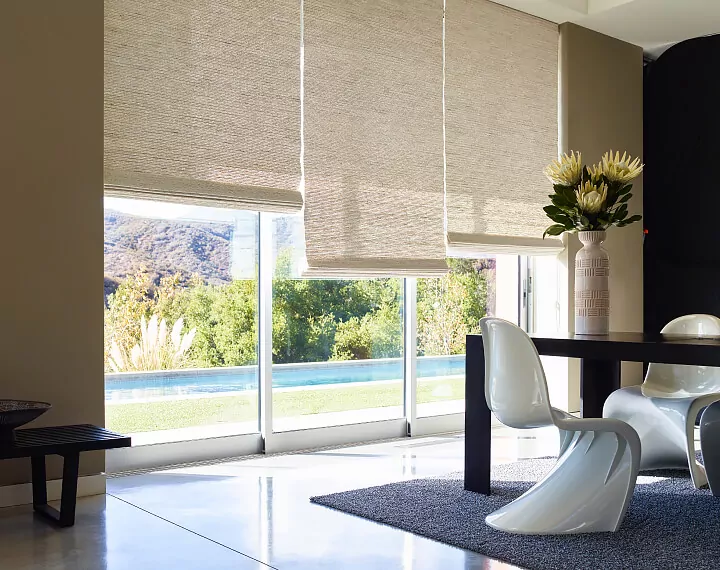 A dining room with modern chairs and sliding glass doors dressed with Woven Wood Shades.