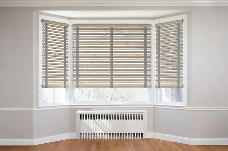 Bay window blinds made of 2-in Bamboo in White with decorative tape in Ash cover a traditional bay window in a sunny room